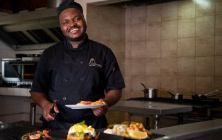 sous-chef-holding-a-plate-of-food-and-smiling-at-the-camera