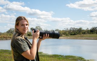 blonde-lady-holding-a-camera-outside-by-a-waterhole