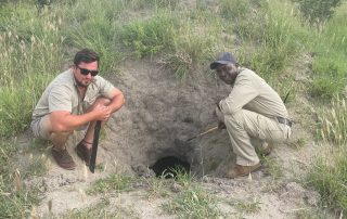 two-men-crouching-next-to-a-termite-mound-hole